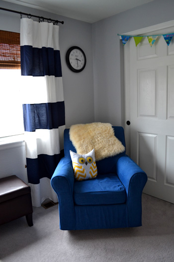 baby boy nursery - navy blue white striped curtains, bamboo blinds, colorful fabric bunting over closet, denim blue slipcover dorel rocking chair, yellow chevron owl pillow, faux leather chocolate ottoman